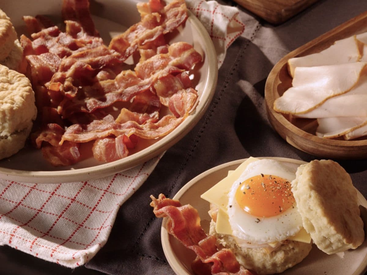A snapshot of a breakfast table set with slicing of Boar's Head® Bacon, an omelette and Boar's Head® cheese sandwich, and a platter with slices of Boar's Head® The Fryer's™ Turkey Breast.